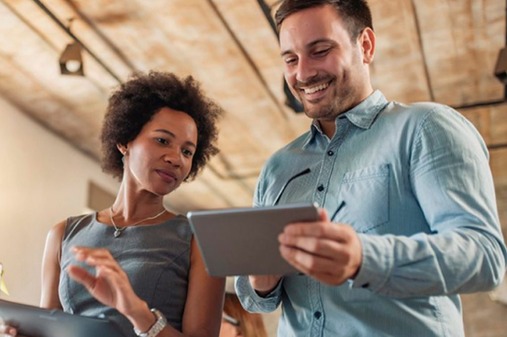 Image depicts two coworkers talking while looking at a tablet computer