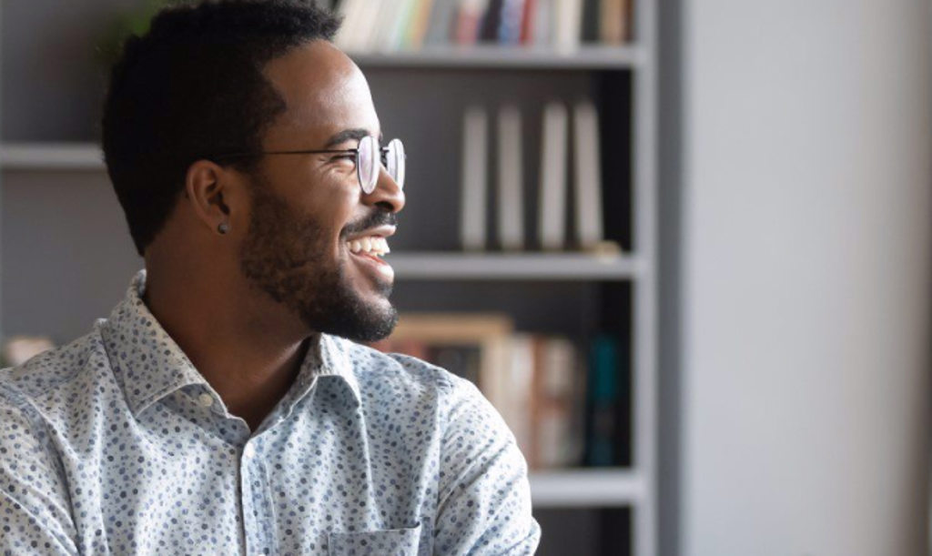 Image depicts a man with glasses smiling and looking off to the right.